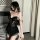 Woman wearing black lace sleepwear set with sheer details and ruffled hem, posing in bedroom setting.