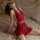 Woman wearing red deep v-neck sleep dress with sheer mesh back, posing on bed in plus size lingerie set.