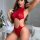 Woman modeling red leopard print lingerie set with cutout design and chain details in bedroom setting.