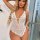 Woman wearing white lace sheer open-crotch bodysuit, sexy sleepwear with floral embroidery and heart detail.