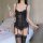 Woman in black lace lingerie set with mesh vest and garter stockings, holding wine glass beside bed with rose petals.