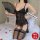 Woman in black lace lingerie set with mesh vest and garter stockings, holding a fan on a bed.
