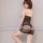 Woman wearing black sheer mesh bodysuit with lace thong and skirt, posing seductively against white wall.