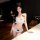 Woman modeling white lace bra and thong set with black bows, provocative uniform-inspired open-crotch design for pure temptat...