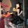 Woman in black pvc catwoman costume with lace-up bodysuit, garter belt, and thong lingerie, holding wine glass at bar.