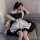 A person wearing a black and white maid costume dress, featuring ruffles and a corset design, sitting on a couch.