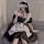 A woman wearing a black and white maid costume dress, featuring ruffles and a crisscross belt detail, sitting on a couch with...