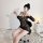Woman wearing sheer black bodycon corset dress with straps, posing in boudoir setting.
