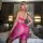 Woman wearing 2800 shiny sheer lingerie set – playful transparent pink intimate wear in bedroom setting.