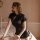 Woman wearing black vintage-style lace corset set with side buckles, retro qipao-inspired lingerie on a bed.