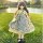 A charming 30cm bjd doll dressed in a floral dress with a green apron, standing on grass near a lake at sunset.