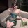 A woman poses elegantly on a couch wearing a luxurious green exotic strapless lingerie set, featuring intricate embroidery an...