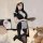 A woman poses wearing a black maid costume with lace details, holding a tray. the outfit features a revealing design and thig...