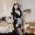 A woman poses wearing a black maid costume with white accents, holding a tray. the outfit features lace details and thigh-hig...