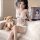 A woman wearing a white lace bodysuit with sheer fabric and open-crotch design sits on a couch next to a teddy bear. the outf...