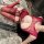 Woman wearing red lace bodysuit with sheer mesh and crotchless design, lying on marble floor.