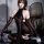 A woman poses wearing a black bodystocking with lace sleeves, featuring sheer design and halter neck style. the outfit highli...