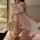 A woman poses on a bed wearing a sheer mesh babydoll dress with lace details, featuring a large bow at the chest and side sli...