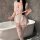 A woman poses in a maid costume, featuring a pink dress with lace details and stockings, holding an umbrella, set against a b...