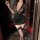 A woman poses elegantly in a black floral lace dress with a deep v neckline, holding a glass. the outfit features sheer sleev...