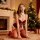 A woman poses in a festive setting wearing a red luxury bodysuit with deep v-neckline, lace details, and fishnet stockings, p...