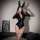 A woman poses with bunny ears, wearing a glossy black catsuit featuring a deep v-neckline and zipper detail. the bodysuit has...