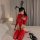A woman poses on a bed wearing a glossy red pvc high-stretch zip-front bodysuit, paired with matching thigh-high boots and bu...
