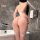 Woman wearing white sheer mesh bodysuit with bow detail and open-crotch design in modern bathroom setting.