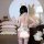 Woman wearing adorable bear maid costume set with plush tail, ears, and cuffs, posing in cozy bedroom with pillows and stuffe...