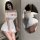 Woman in white ai ruru lingerie strap dress with sheer mesh, off-shoulder cutout design, posing by mirror.