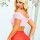 Blonde woman wearing a pink off-shoulder lace crop top with ruffled sleeves, paired with a red skirt, posing against a floral...