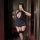 Woman in navy blue avian moon sheer airline-themed bodycon skirt set with garter straps, holding wine glass and phone.