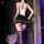 A woman stands with her back to the camera, wearing a white top and black skirt with ruffles. she has stockings on and holds ...