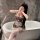 Woman in bird moonling lingerie set, a seductive maid costume with plaid dress and white apron, sitting on bathtub edge.