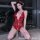 Woman wearing red lace mesh bodysuit with deep v neck and halter straps, posing in front of city lights at night.