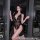 Woman wearing black lace mesh bodysuit with deep v neck and halter straps, posing on a balcony at night.