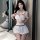 A woman poses wearing a white sailor uniform lingerie set featuring a bow top and skirt, paired with fishnet stockings, ideal...