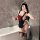 A woman poses in a bathroom wearing a black maid costume with red bows, featuring a backless apron and stockings, holding a g...