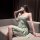 Woman in elegant green lace lingerie set with sheer cami and matching briefs, posing seductively on sofa.