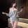 Woman wearing chaomu sensual lingerie dress, one-shoulder backless cutout bodycon mini dress in soft gray, posing with phone.