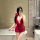 Woman in red cherry blossom lingerie set with sheer mesh, halter neck, and backless design, posing by a bathtub.