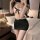 Woman modeling cherry romance lingerie set: white lace top with black bow, black mini skirt, in bedroom setting.