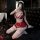 Woman in red cherry romance lingerie set with lace bra, open-crotch skirt, and thigh-highs, posing on black leather bed.