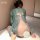 A woman sits on the floor wearing a sheer green hanfu-style crop dress over a white bralette, holding a decorative fan. the o...