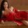 A woman lounges on a couch wearing a vibrant red chinese-inspired transparent lace lingerie set, featuring delicate patterns ...
