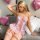 A woman poses elegantly in a sheer pink bodysuit adorned with lace, bows, and cut-outs, perfect for romantic evening wear.