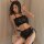 Woman modeling black devil-themed lingerie set with red heart details, open-bust top, lace shorts, and horn headband.