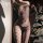 Woman wearing domoila irregular mesh sheer leopard bodysuit with backless lace-up design, posing beside a christmas tree.