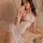 A woman poses elegantly wearing a sheer mesh lace bodysuit with halter straps, featuring delicate heart patterns and pearl ac...