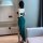 Woman wearing emerald green backless dress with high slit, showcasing elegant silhouette in modern interior setting.